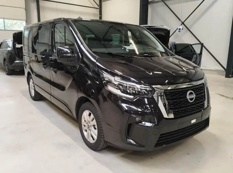 Nissan Primastar noir vue 3/4 avant droit dans un garage, avec calandre chromée et phares LED distinctifs.