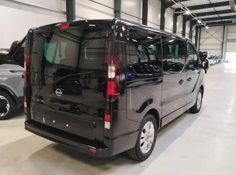 Vue 3/4 arrière droite d’un Nissan Primastar noir avec portes latérales, stationné en intérieur lumineux.