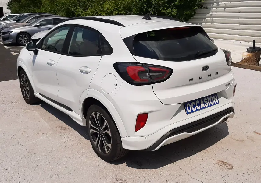Vue 3/4 arrière droite d'un Ford Puma blanc 2022 avec toit noir et jantes alliage, garé sur un parking extérieur.