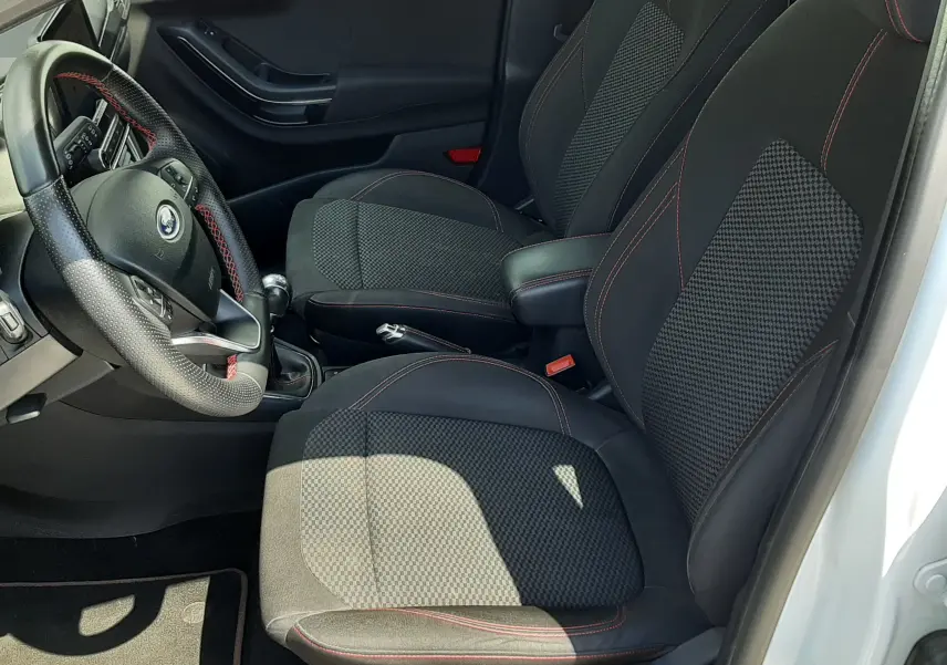 Vue intérieure côté conducteur du Ford Puma blanc 2022, sièges tissu noir avec surpiqûres rouges et volant cuir.