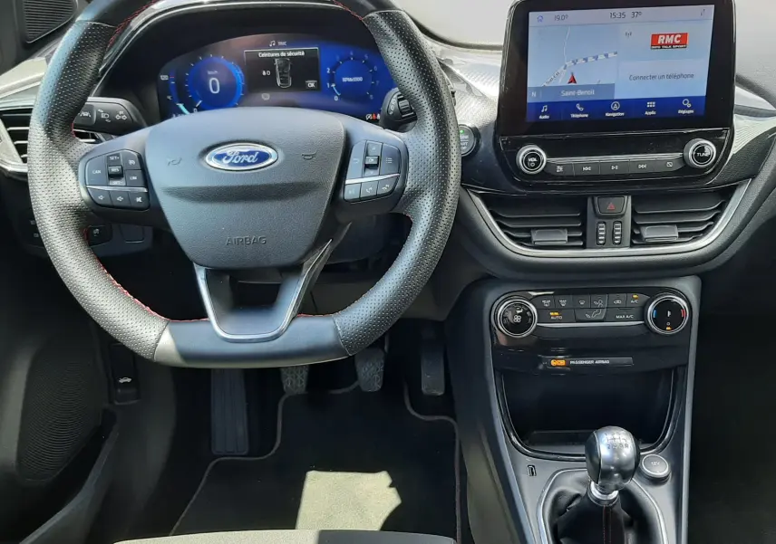 Vue intérieure du tableau de bord et volant noir perforé du Ford Puma blanc 2022, avec écran tactile et boîte manuelle.