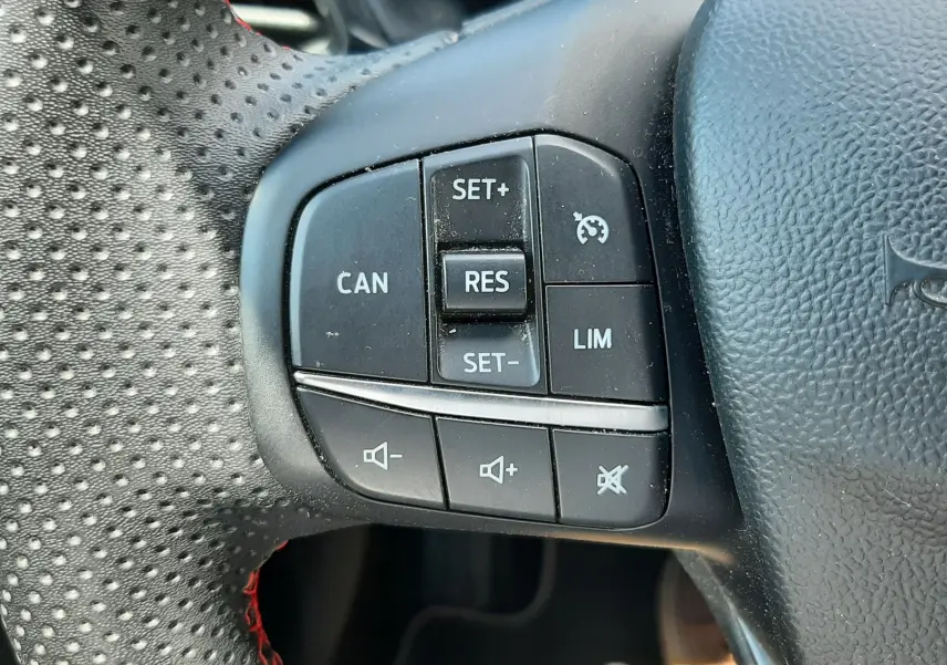 Gros plan sur les commandes de régulateur de vitesse et volume au volant perforé noir avec surpiqûres rouges du Ford Puma blanc 2022.