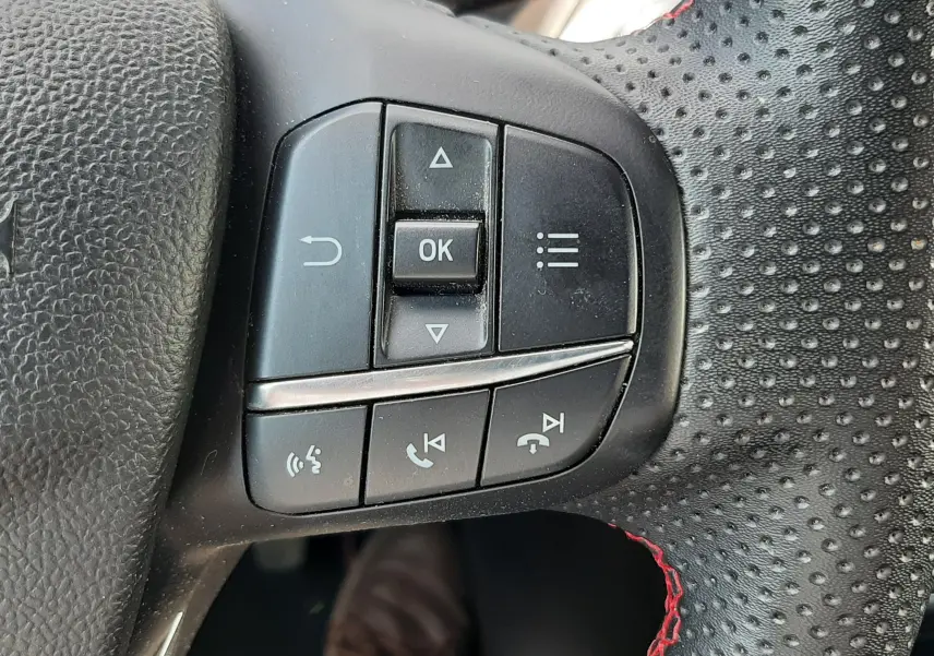 Gros plan sur les commandes multifonctions du volant perforé avec surpiqûres rouges du Ford Puma blanc 2022.