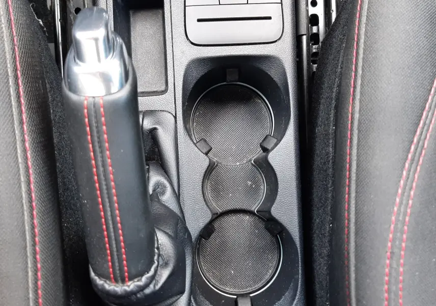 Vue rapprochée de la console centrale noire du Ford Puma 2022, avec frein à main cuir noir surpiqué rouge et porte-gobelets doubles.