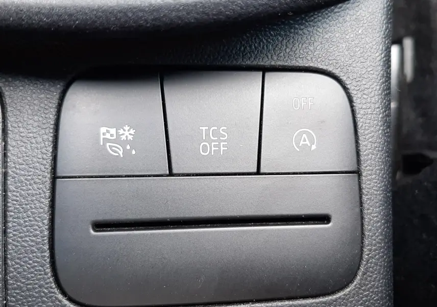 Gros plan sur les boutons de commande noirs du tableau de bord du Ford Puma blanc, avec symboles d'assistance et désactivation.