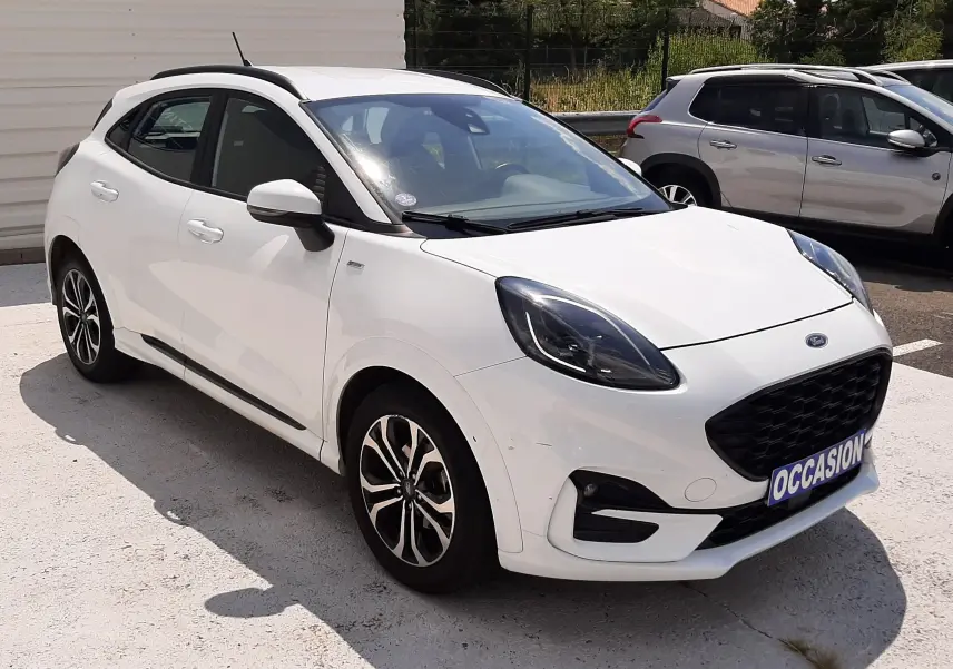 Ford Puma blanc en 3/4 avant droit, avec calandre noire et jantes alliage bicolores, stationné en extérieur.