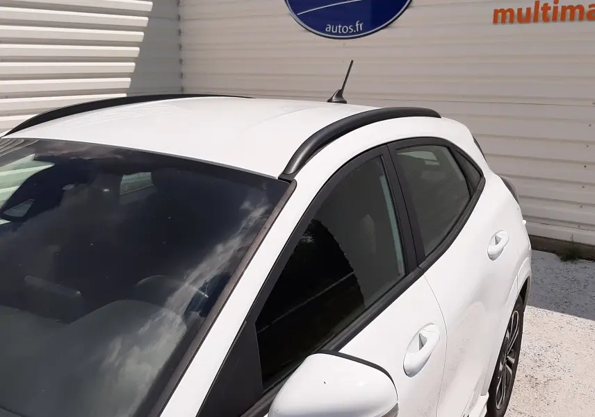 Vue 3/4 avant droit du Ford Puma blanc 2022 ST-LINE avec barres de toit noires et vitres teintées.