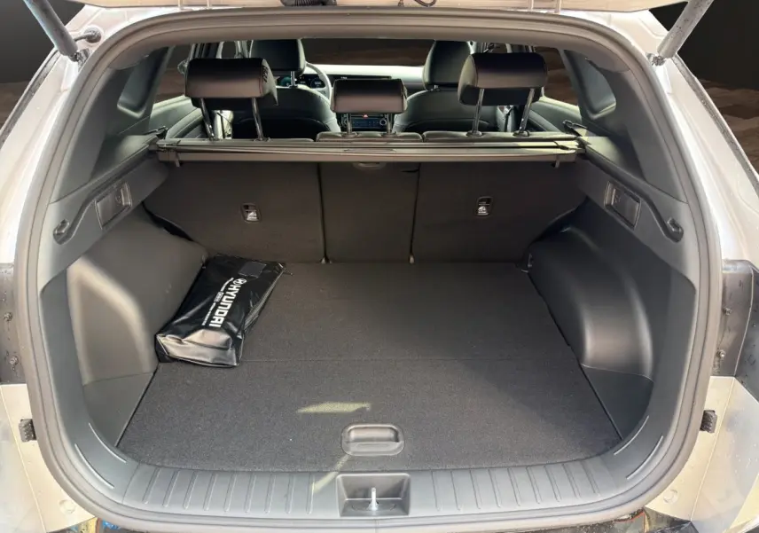 Vue arrière du coffre ouvert d’un Hyundai Tucson gris clair, avec housse d’accessoires Hyundai posée à gauche.