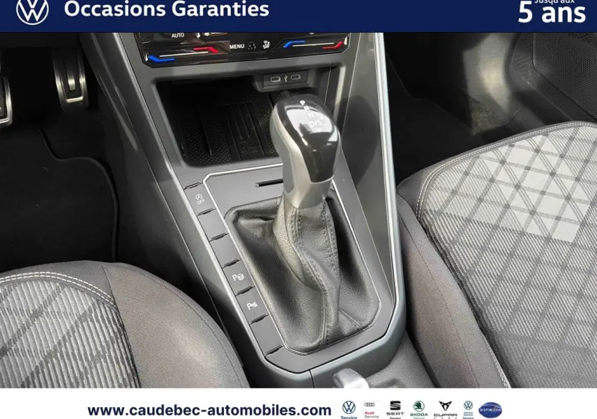 Gros plan sur la console centrale et levier de vitesse manuel d’une Volkswagen Polo rouge, sièges à motifs gris visibles.