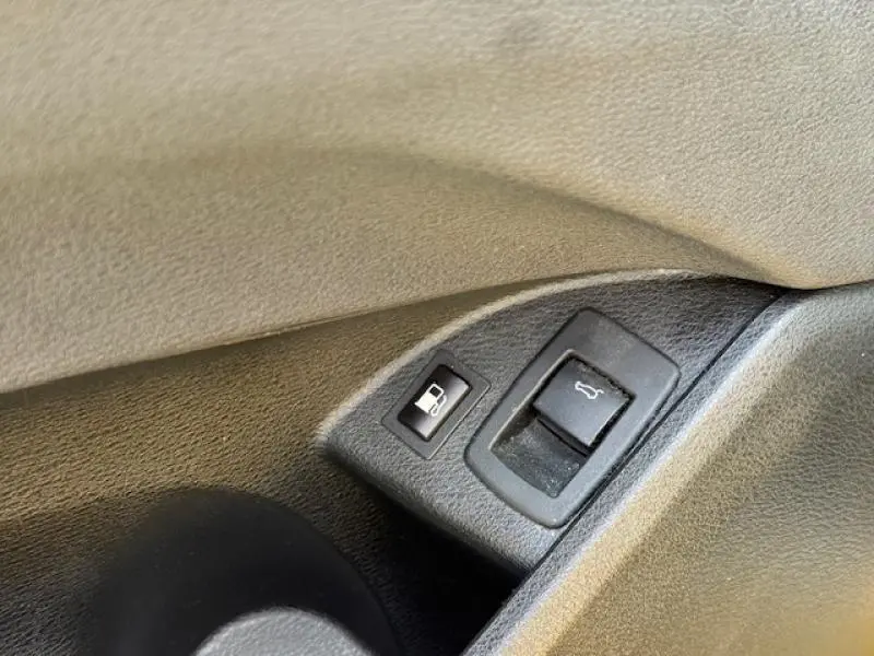 Boutons d'ouverture de trappe à carburant et coffre sur le côté gauche intérieur d'une BMW X2 Galvanic Gold.