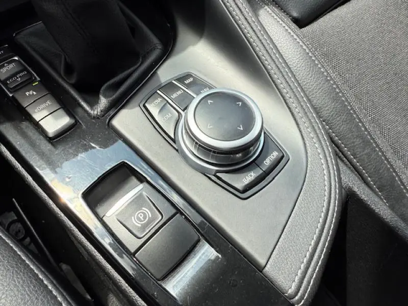 Gros plan sur la molette de commande multimédia et frein à main électronique dans l'habitacle noir du BMW X2 Galvanic Gold.