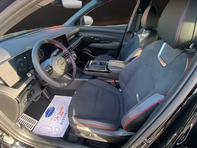Vue intérieure côté conducteur du Hyundai Tucson noir 2026, sièges noirs avec surpiqûres rouges et tableau de bord digital.