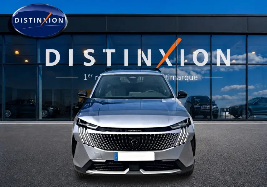 Vue frontale d'un Peugeot 5008 Hybrid 145 allure e-dcs6 gris artense devant une vitrine Distinxion.