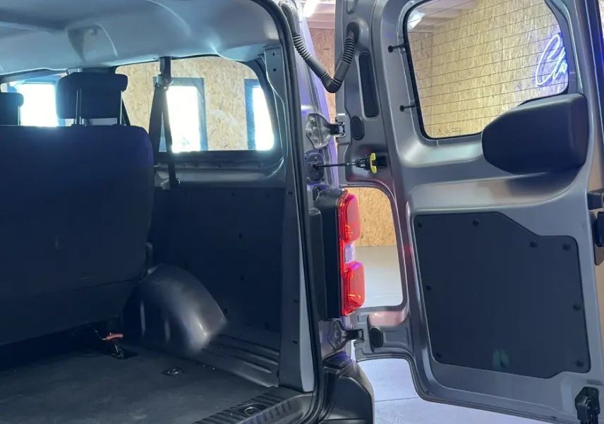 Vue intérieure arrière du gris Opel Vivaro Combi 1.5 Diesel 120 avec porte arrière ouverte et sièges en tissu noir.