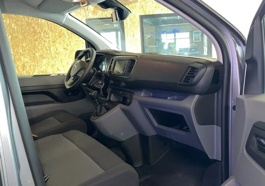 Intérieur avant droit de l'Opel Vivaro Combi gris 2022, avec tableau de bord et sièges en tissu noir.