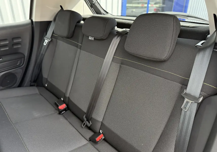 Vue intérieure arrière montrant la banquette noire et grise avec ceintures de sécurité de la Citroën C3 gris platinium 2024.