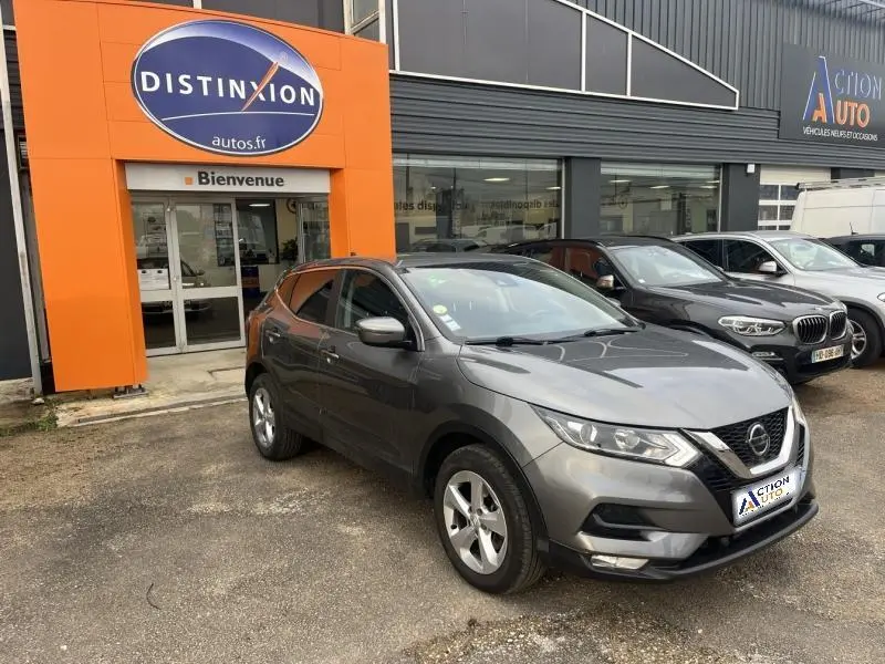 Nissan Qashqai gris Squale en 3/4 avant droit, garé devant un concessionnaire avec logo Distinxion visible.