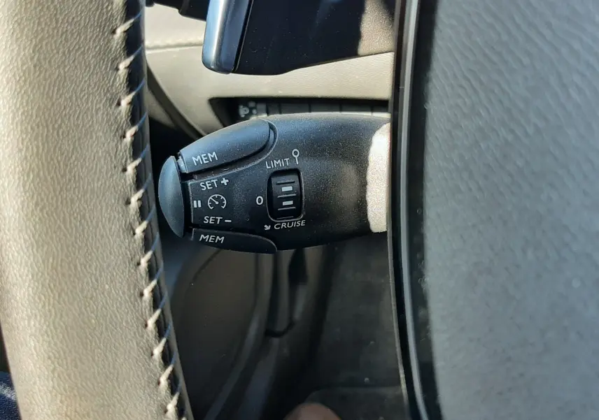 Gros plan sur la commande de régulateur de vitesse noire à gauche du volant gris du Peugeot 2008 Hybrid 145 Allure.