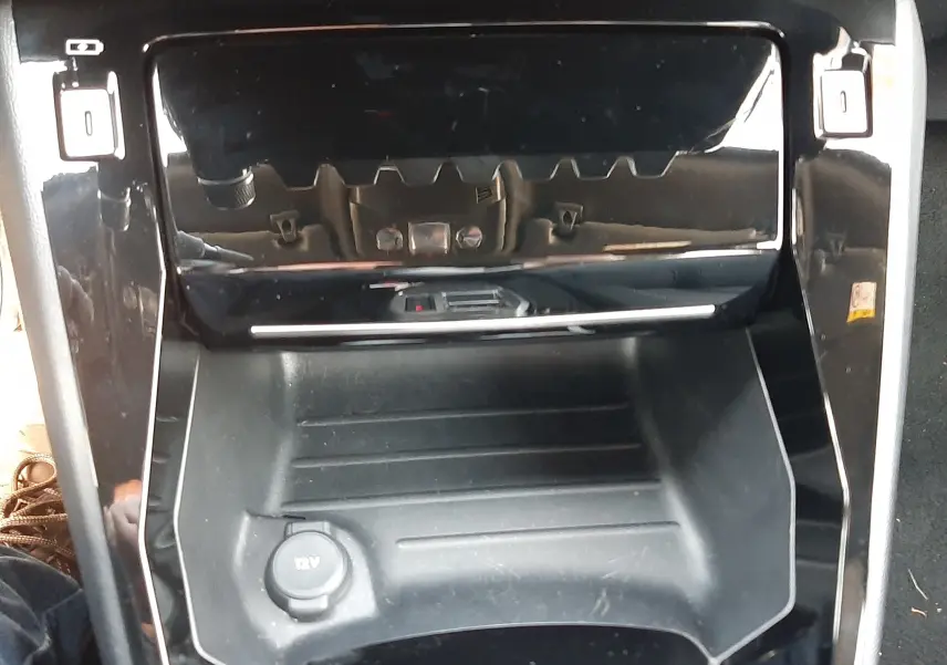 Gros plan sur la console centrale noire brillante du Peugeot 2008 Hybrid 145 Allure, avec prise 12V visible.