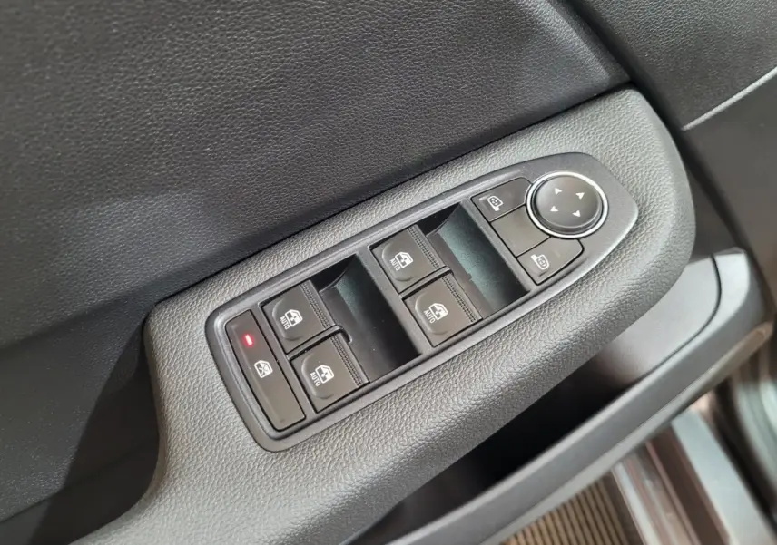 Gros plan sur la commande des vitres électriques et rétroviseurs sur la portière côté conducteur d'une Renault Clio gris foncé.