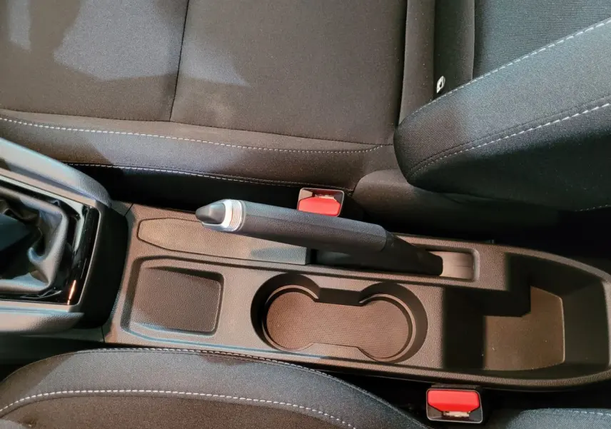 Vue intérieure rapprochée du frein à main manuel et porte-gobelets entre les sièges noirs de la Renault Clio gris foncé.