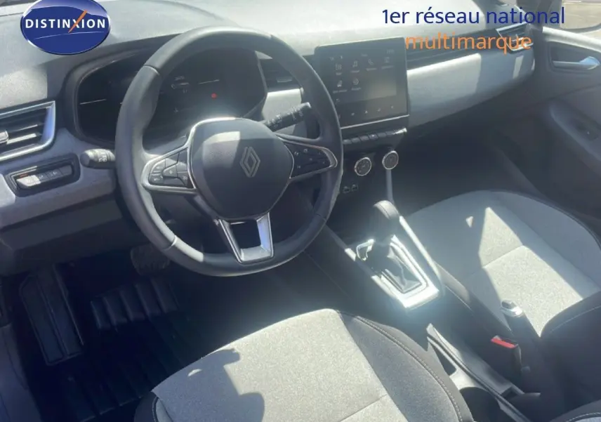 Vue intérieure avant de la Renault Clio 2025, volant multifonction, sièges tissu gris et console centrale avec écran tactile.