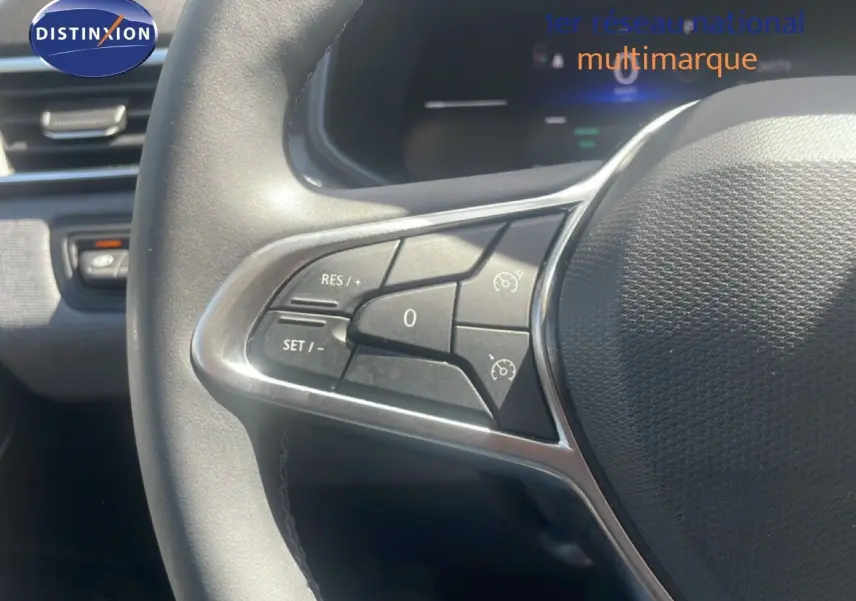Gros plan sur les commandes au volant côté gauche de la Renault Clio blanche, mettant en valeur les boutons de régulateur de vitesse.