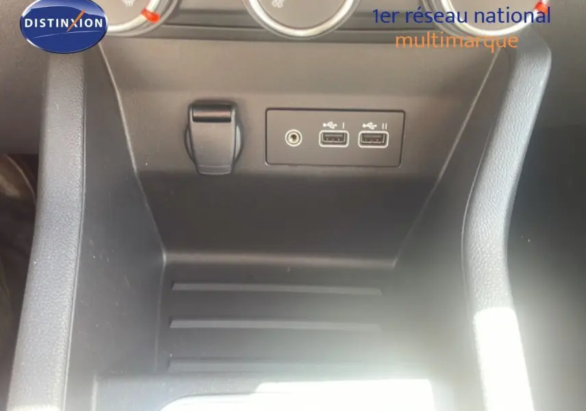 Vue rapprochée de la console centrale noire de la Renault Clio blanche, montrant les ports USB et la prise auxiliaire.