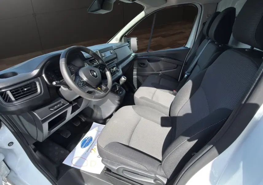 Vue intérieure côté conducteur du Renault Trafic Fourgon blanc 2024, montrant le tableau de bord et les sièges tissu gris.