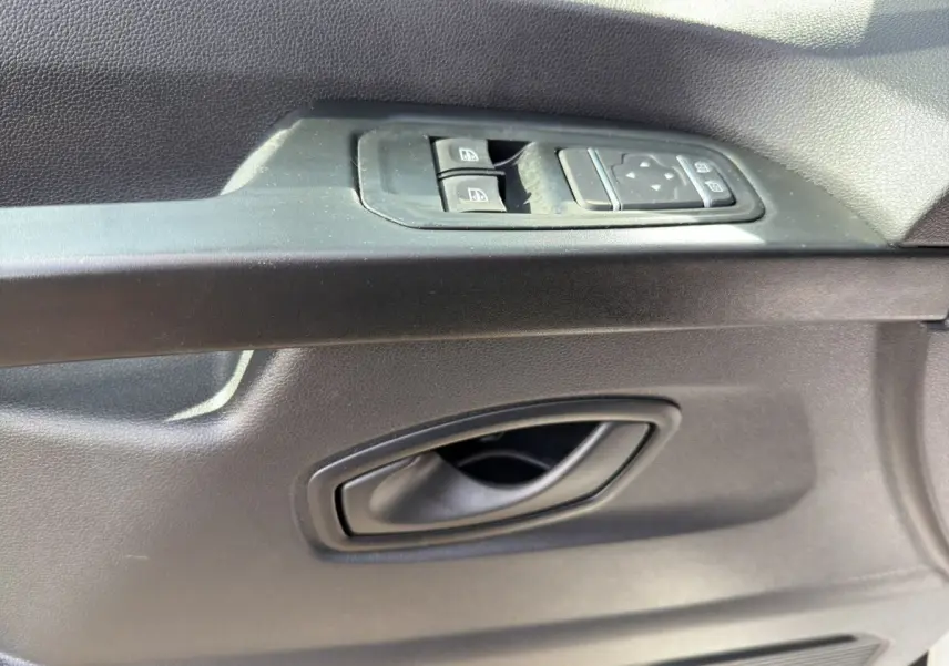 Gros plan sur la poignée intérieure et les commandes des vitres côté conducteur du Renault Trafic Fourgon blanc.