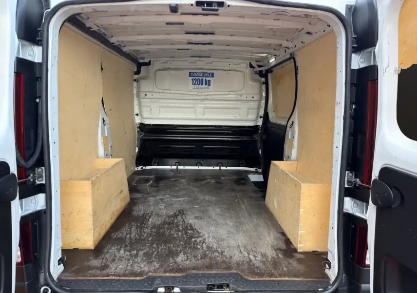 Vue arrière du fourgon Renault Trafic blanc 2024, montrant l’espace de chargement avec protections en bois sur les côtés.