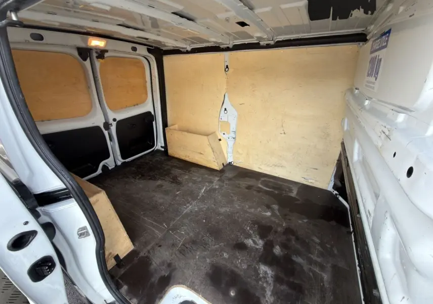 Vue intérieure arrière du fourgon blanc Renault Trafic avec cloison et plancher en bois, montrant l'espace de chargement vide.