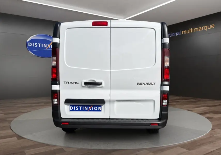 Vue arrière du fourgon blanc Renault Trafic avec portes battantes et feux verticaux rouges, en showroom.