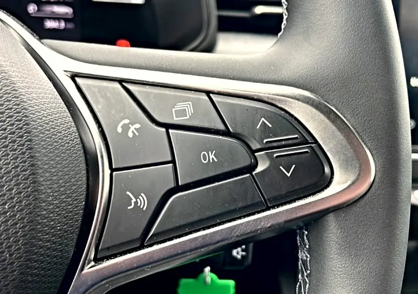 Gros plan sur les commandes multifonctions noires du volant côté gauche d’une Renault Clio V blanche.