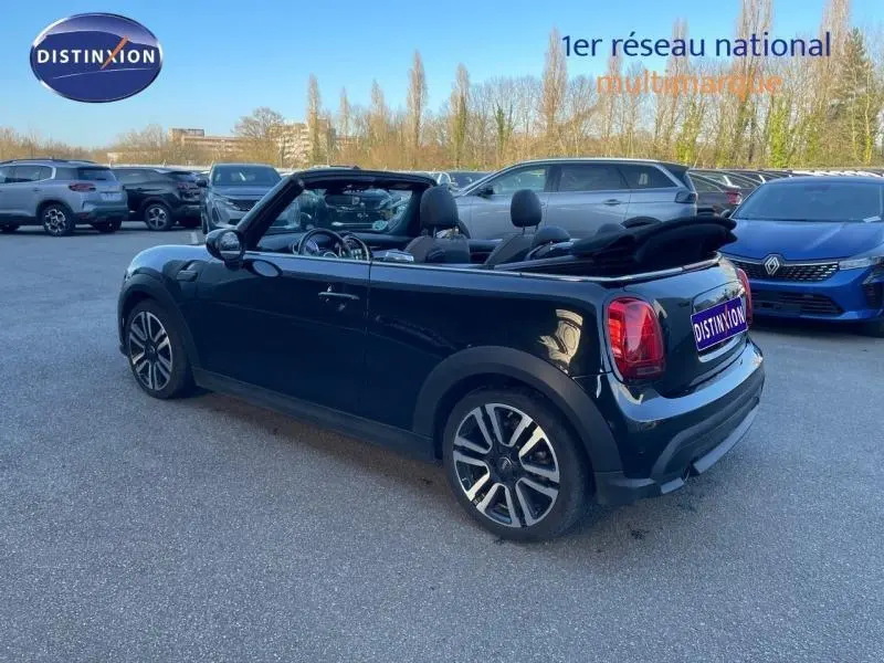 Vue 3/4 arrière droite d'une MINI Cabriolet Cooper noire avec capote souple ouverte sur parking.