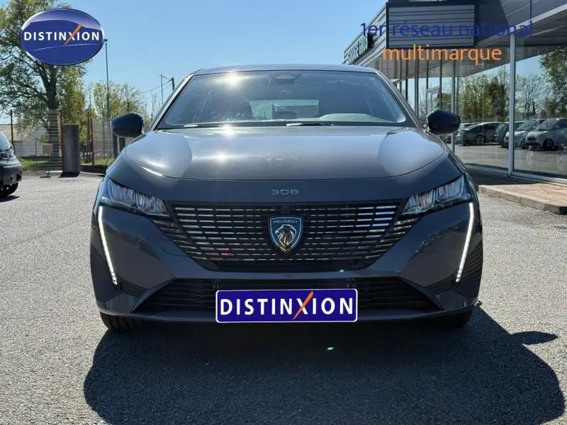 Vue avant d'une Peugeot 308 gris métallisé 2025 avec calandre noire et feux LED verticaux allumés.
