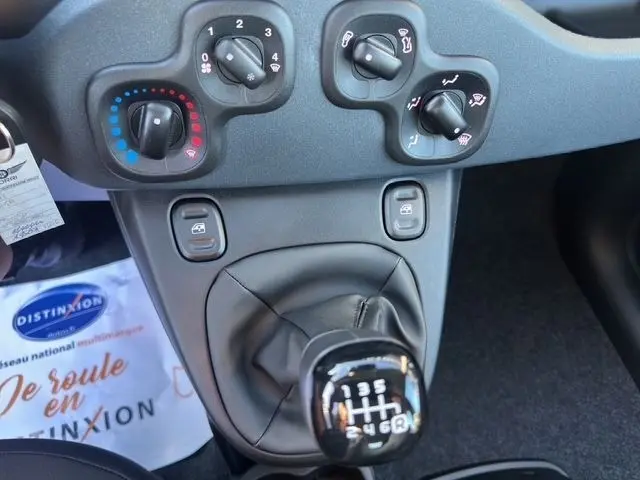 Vue rapprochée de la console centrale de la Fiat Panda noire 2025, mettant en valeur le levier de vitesse manuel et les commandes de climatisation.