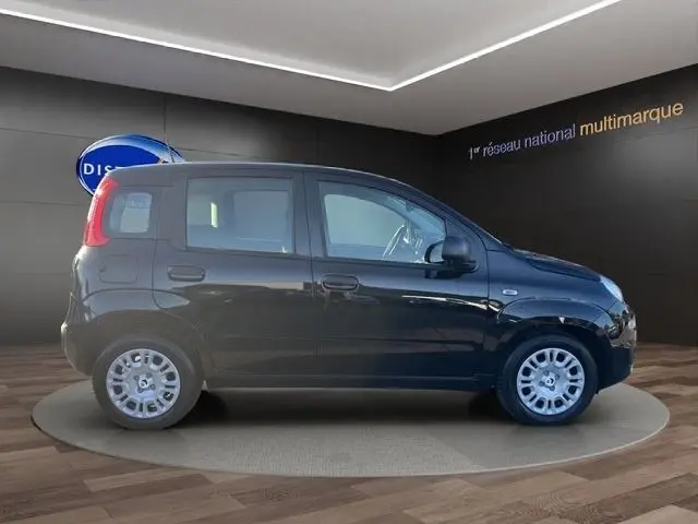 Vue de profil côté gauche d'une FIAT Panda noire 2025 exposée en intérieur sur un podium circulaire.