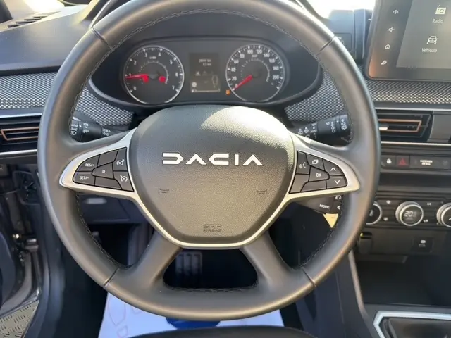 Vue rapprochée du volant en cuir synthétique noir de la Dacia Sandero Stepway 2025, avec tableau de bord et écran tactile visibles.
