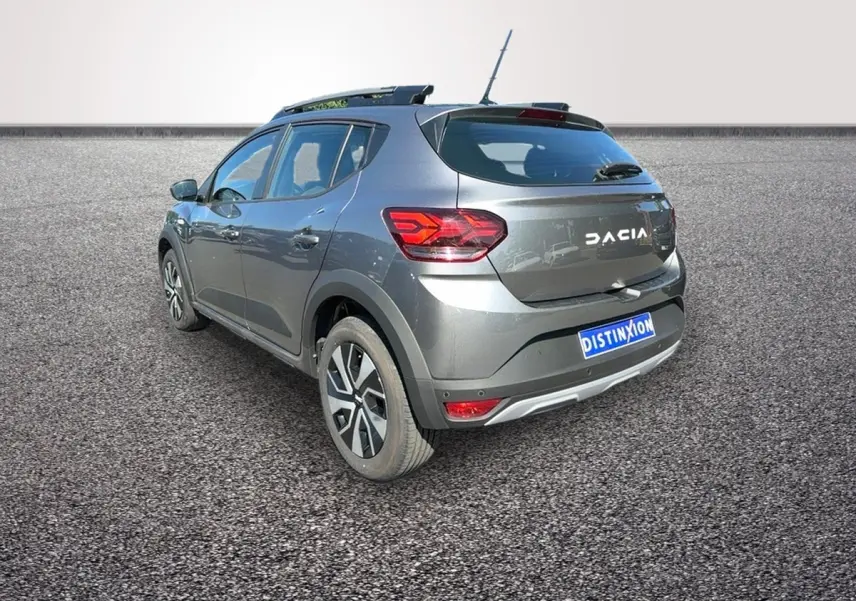 Vue 3/4 arrière droite d'une Dacia Sandero Stepway gris foncé avec barres de toit et jantes distinctives.