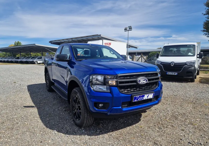 Ford Ranger Super Cabine bleu Lightning en 3/4 avant droit sur parking gravillonné, avec plaques Zero KM visibles.