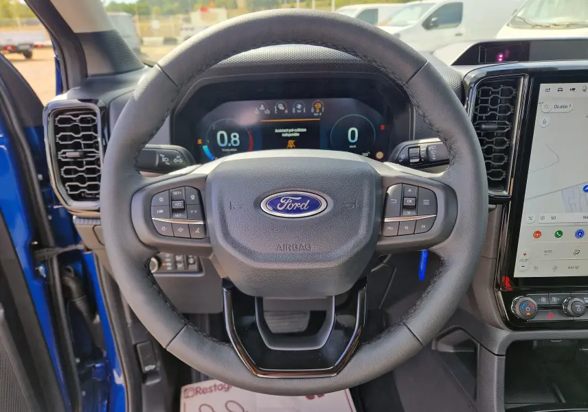 Vue intérieure centrée sur le volant du Ford Ranger Super Cabine bleu Lightning avec tableau de bord numérique et écran tactile.