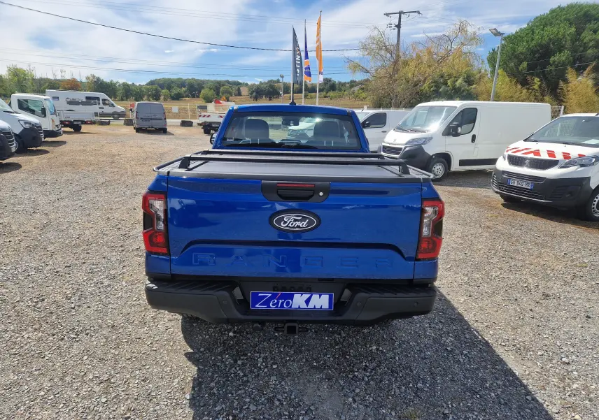 Vue arrière d'un Ford Ranger Super Cabine bleu Lightning avec rideau de plateau rigide et attelage visible.