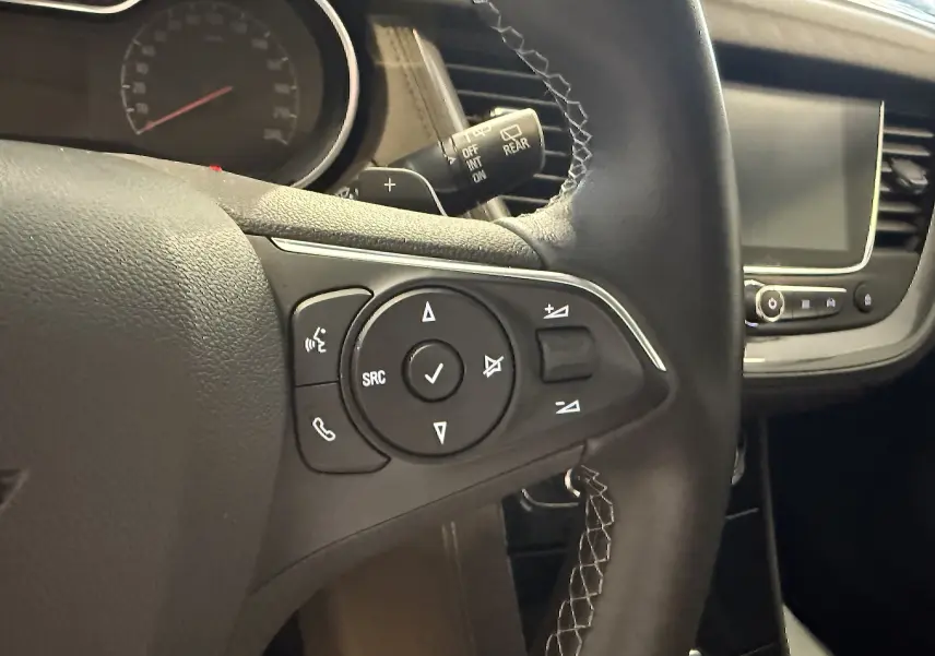 Gros plan sur le volant gauche de l’Opel Grandland X gris Himalaya, avec commandes audio et écran tactile visible.