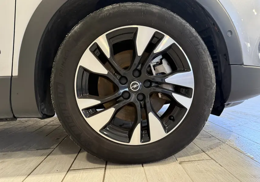 Gros plan sur la roue avant droite d'un Opel Grandland X gris Himalaya avec jante alliage bicolore et logo Opel central.