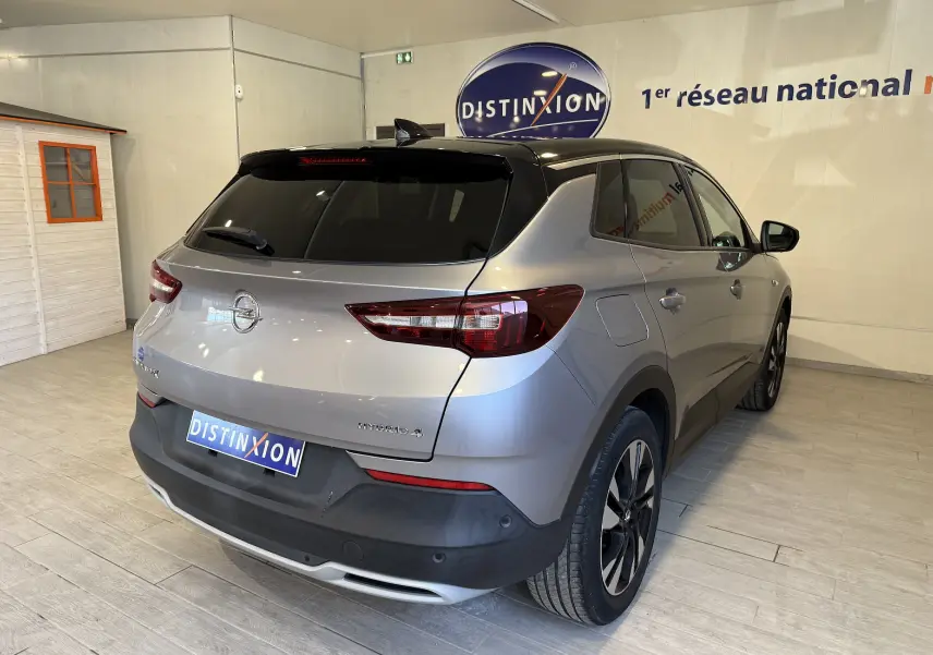 Vue 3/4 arrière droite d'un Opel Grandland X gris Himalaya métallisé avec toit noir et jantes alliage en showroom.