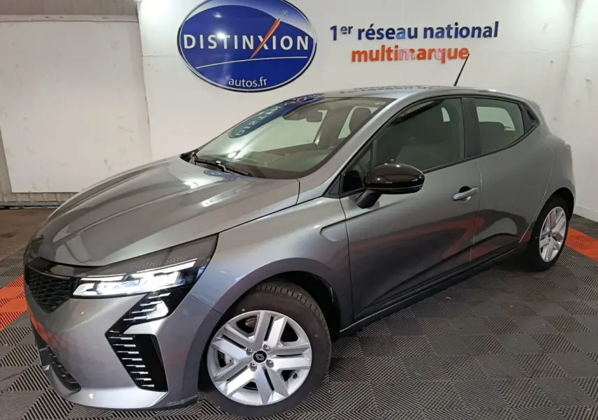 Renault Clio Evolution Blue dCi 100 gris clair vue 3/4 avant droit avec phares LED allumés en intérieur showroom.