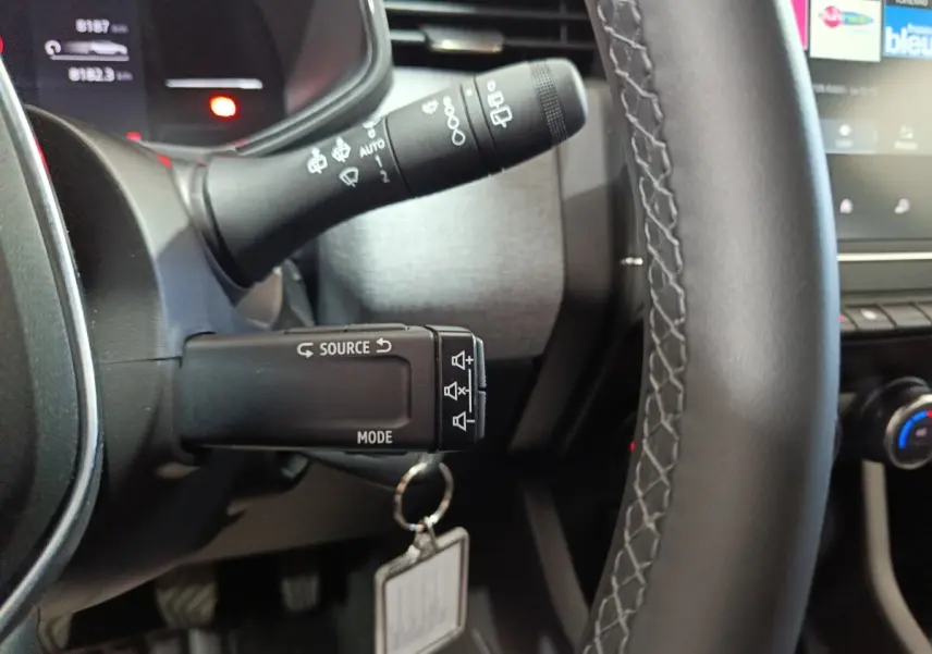 Gros plan sur le volant cuir synthétique et les commandes multifonctions à gauche du tableau de bord de la Renault Clio gris clair.