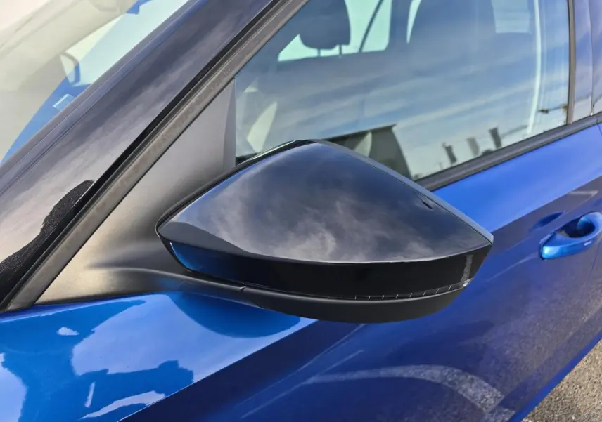 Gros plan sur le rétroviseur côté gauche noir brillant d’un Skoda Kamiq bleu racing avec toit noir.