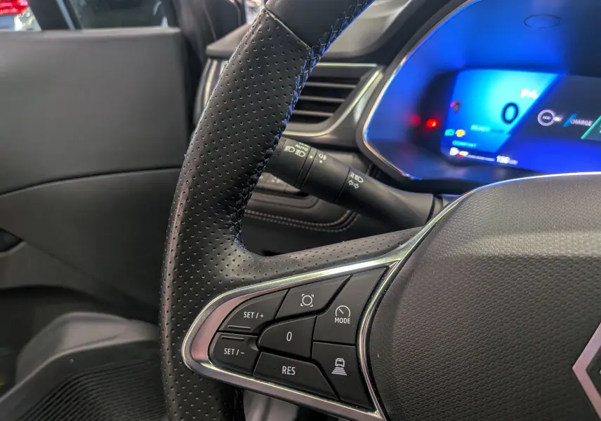 Gros plan sur le volant en cuir perforé et le tableau de bord numérique bleu du Renault Symbioz Gris Cassiopé, version hybride 2025.